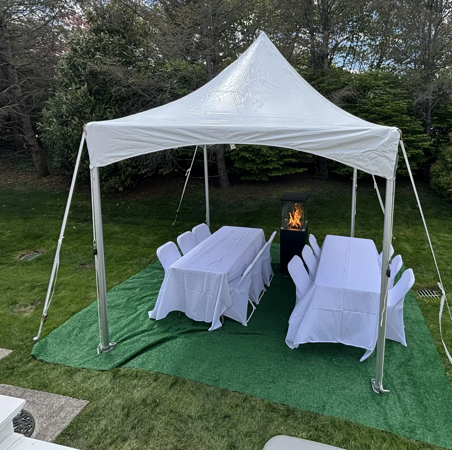 White 10 by 10 high-peak tent with banquet tables, chair covers and a patio heater