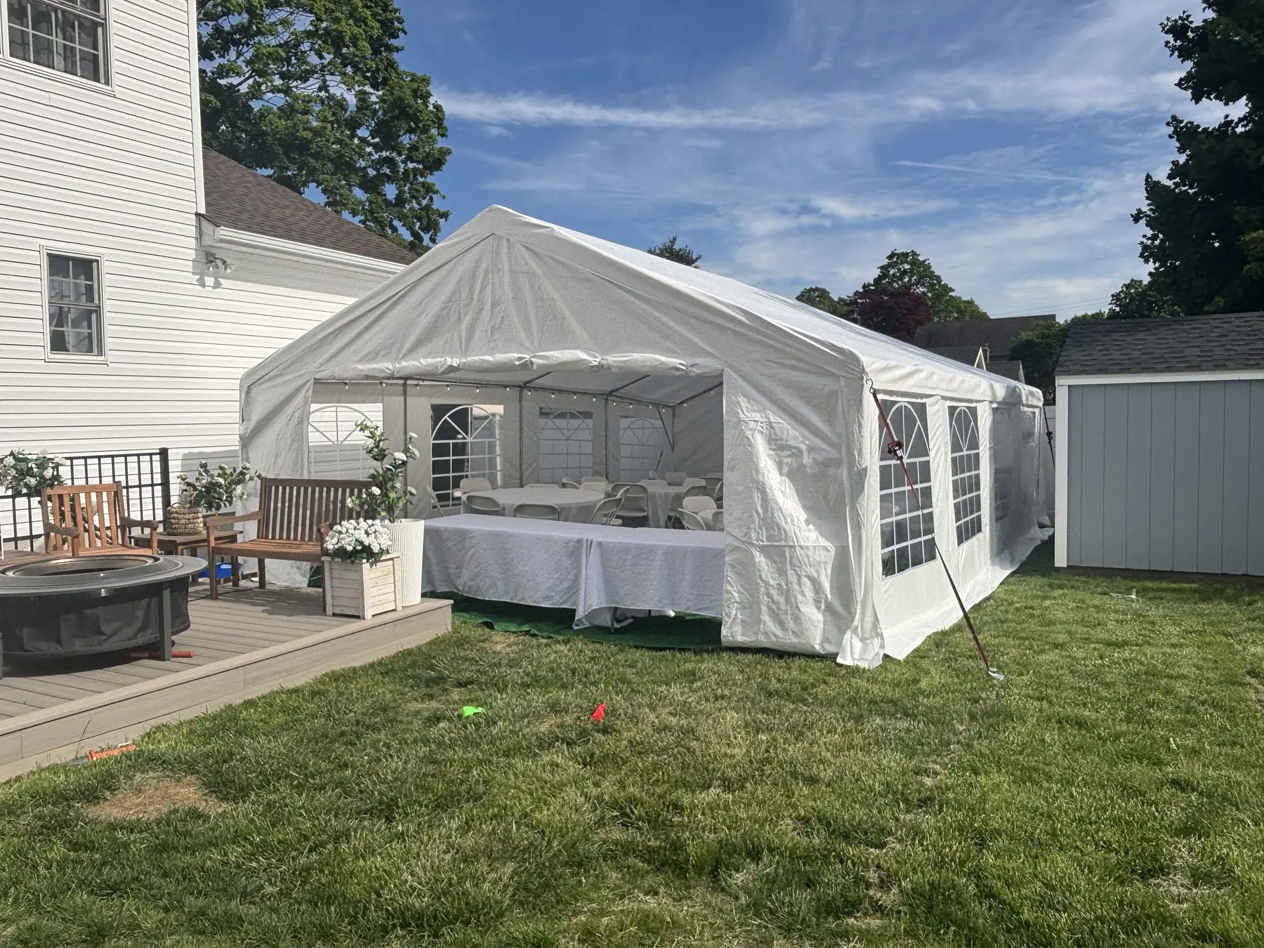 White frame tent with window sidewalls, banquet tables and string lights in a backyard