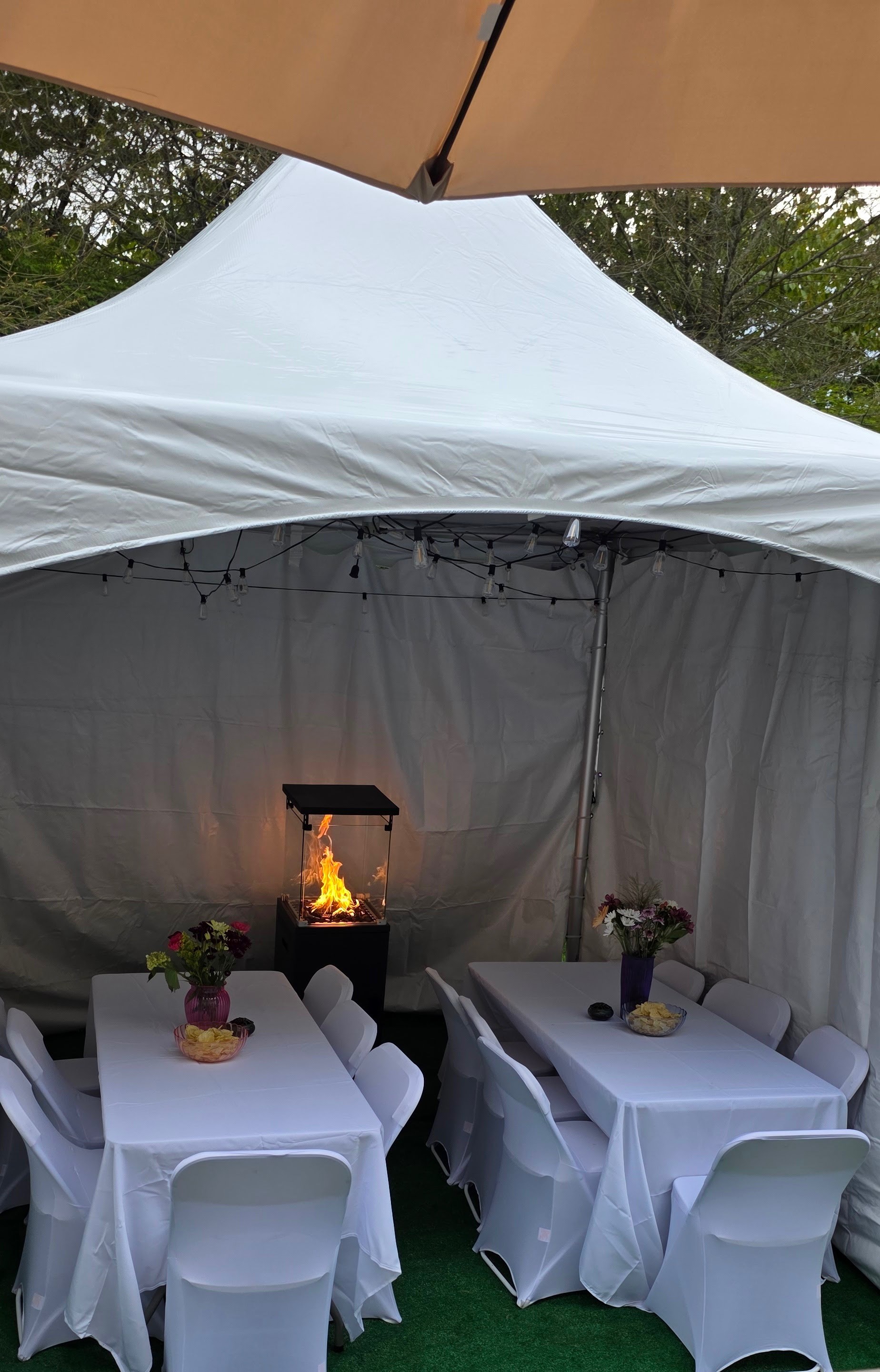 Custom tent setup on a condominium deck with banquet tables, white chair covers and string lights