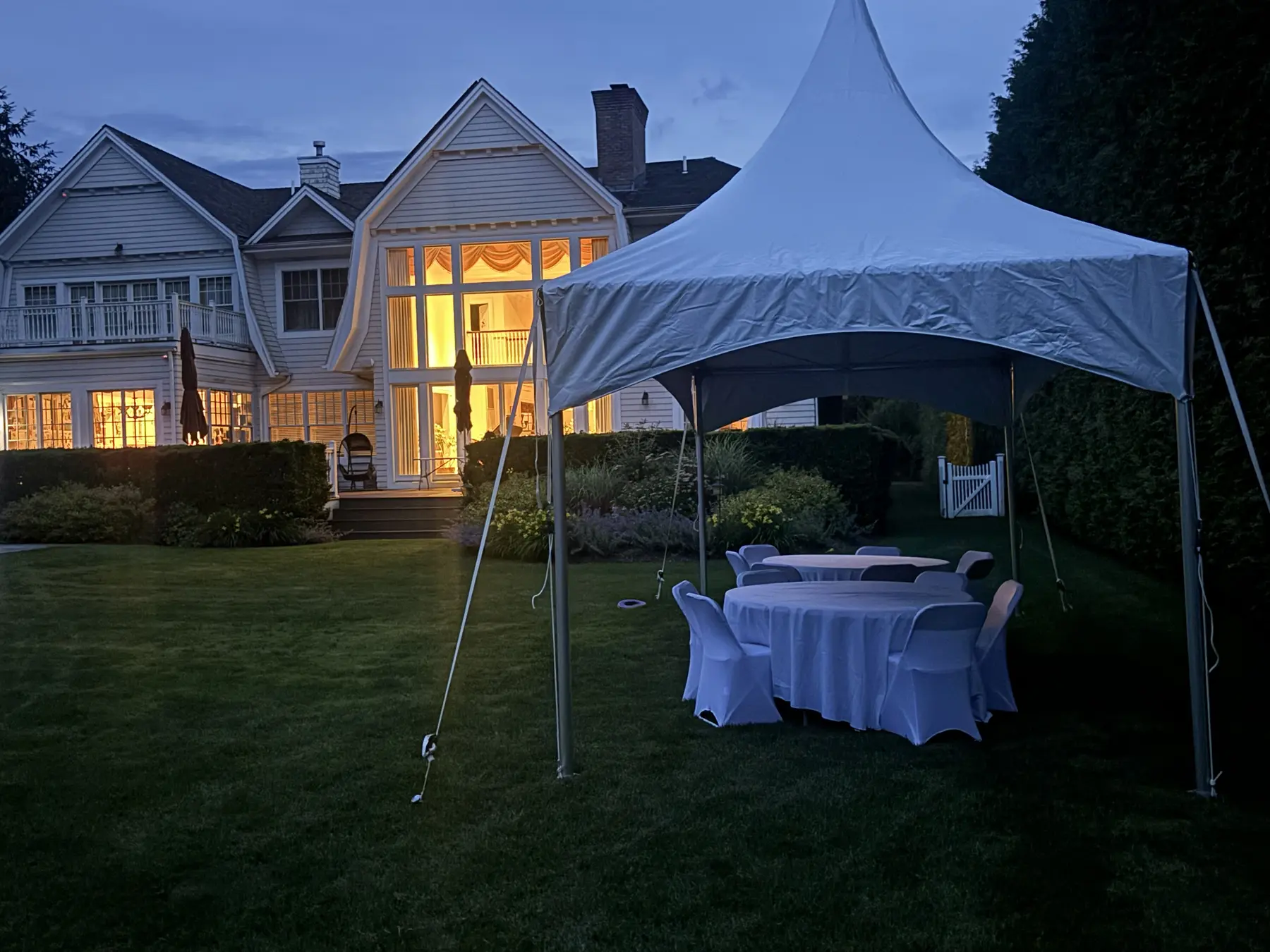 High-peak tent with round tables set up on a lawn at dusk