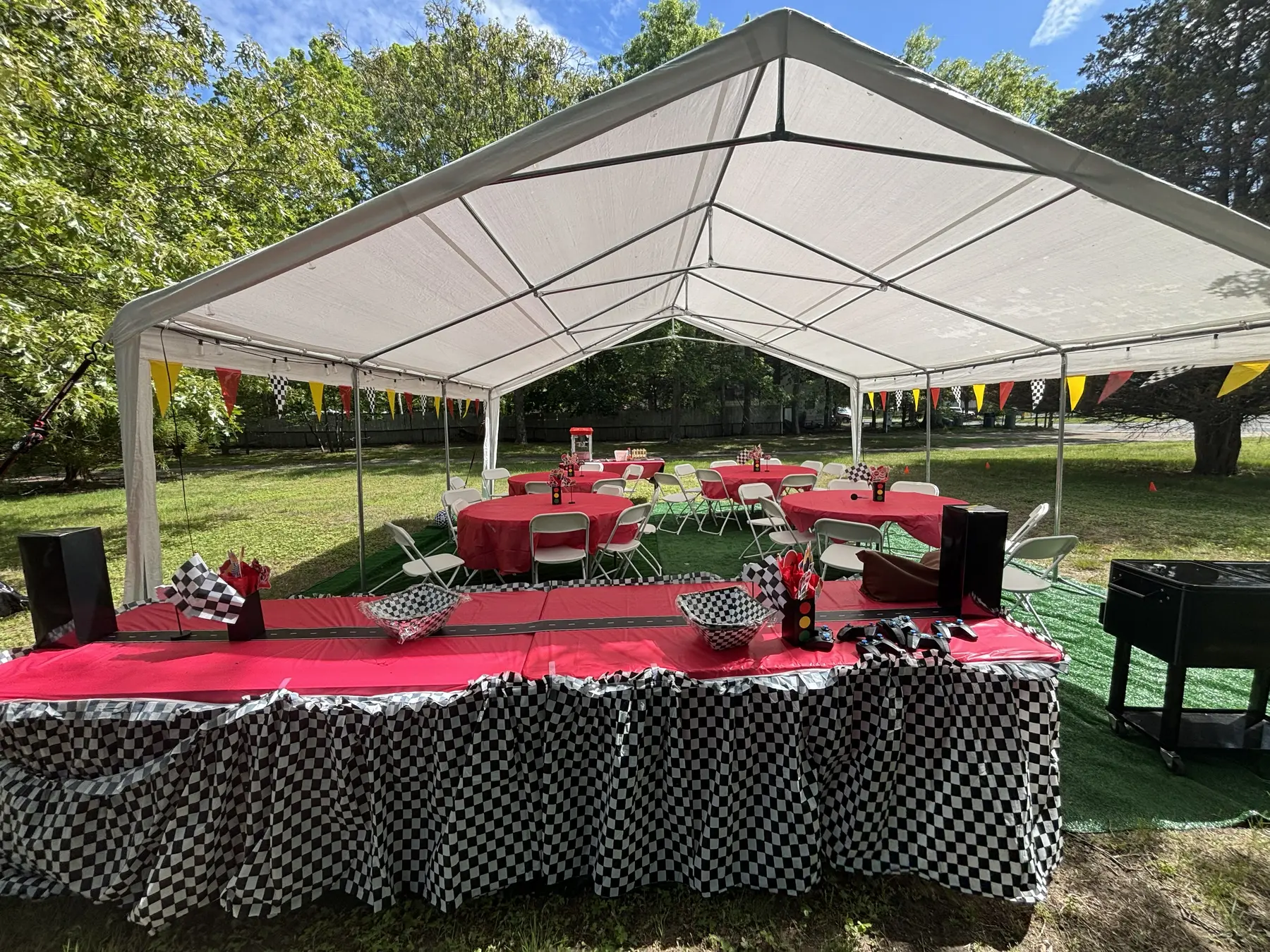 Racing-themed party inside a white frame tent with red tables and checkered decorations