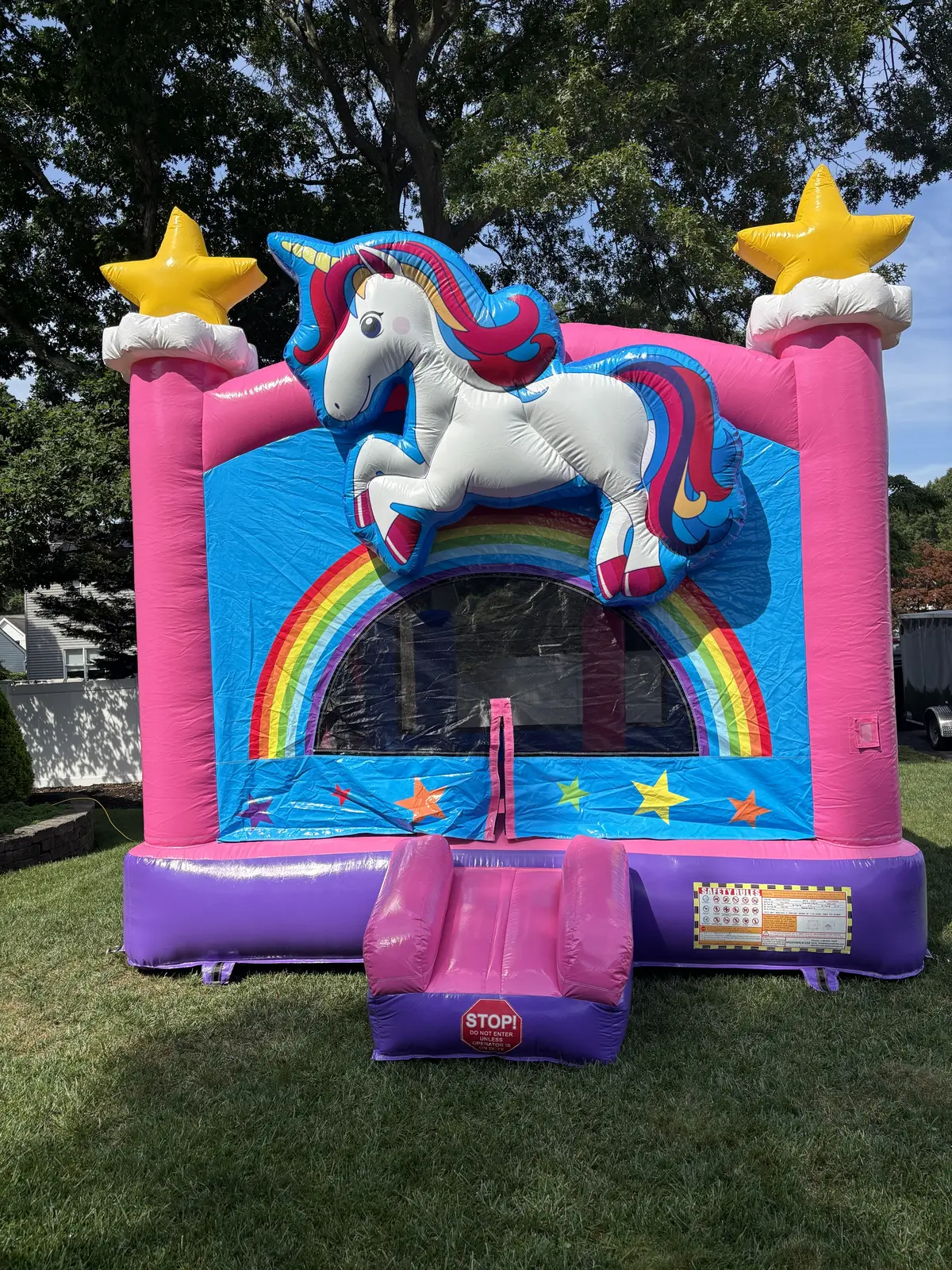Pink and blue unicorn and stars bounce house set up on a sunny backyard lawn