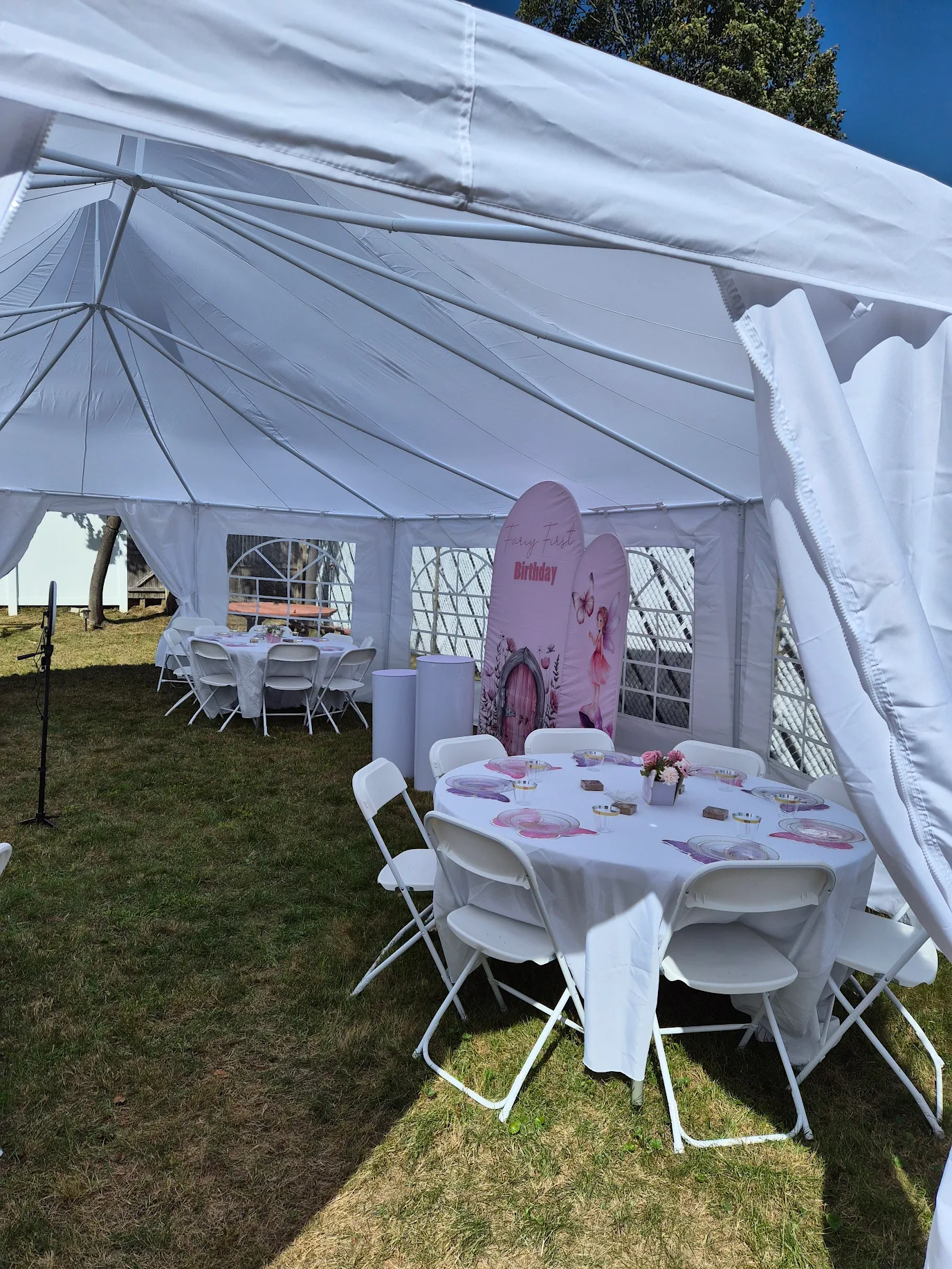 Tent interior set up for a first birthday party with round tables and white chairs